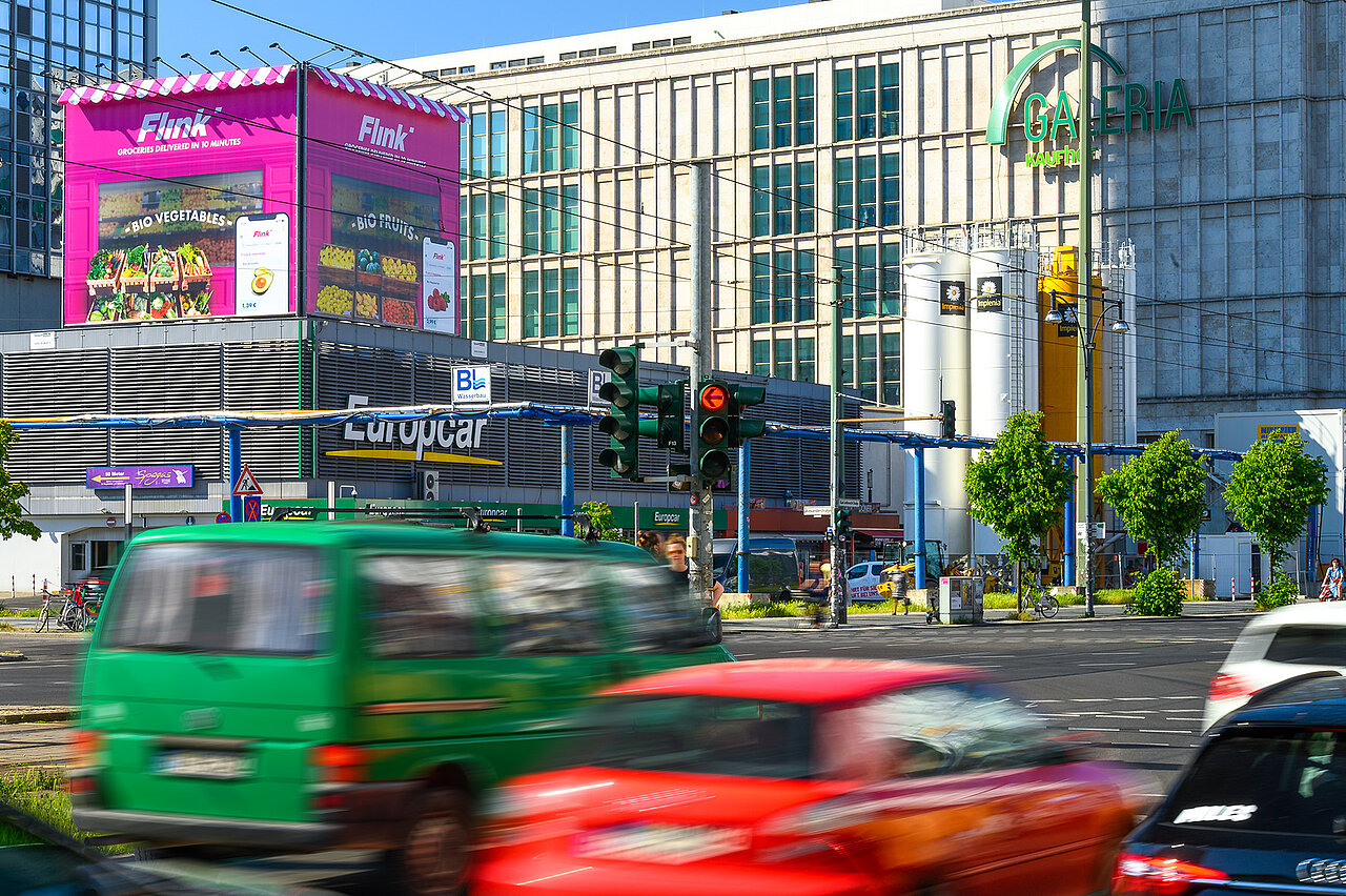Großformatige Flink-Werbeinstallation im Stil eines übergroßen Kiosks auf einem Berliner Dach, umgeben von stark befahrener Kreuzung und vorbeifahrenden Autos.