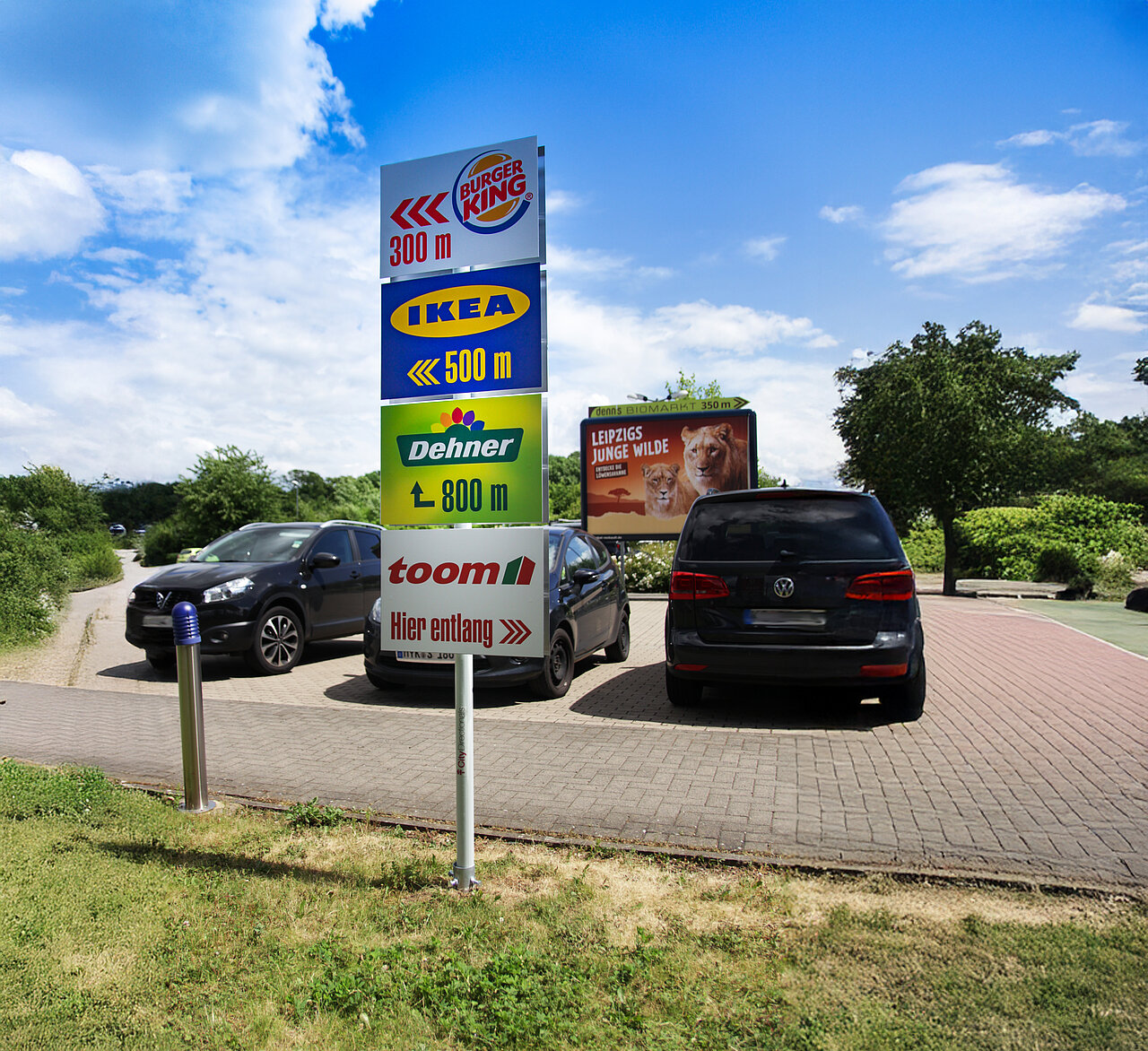 Werbeschilder an einer Straße zeigen Entfernungen zu verschiedenen Geschäften wie Burger King, IKEA und Dehner. Das Schild weist den Weg zu den verschiedenen Standorten.