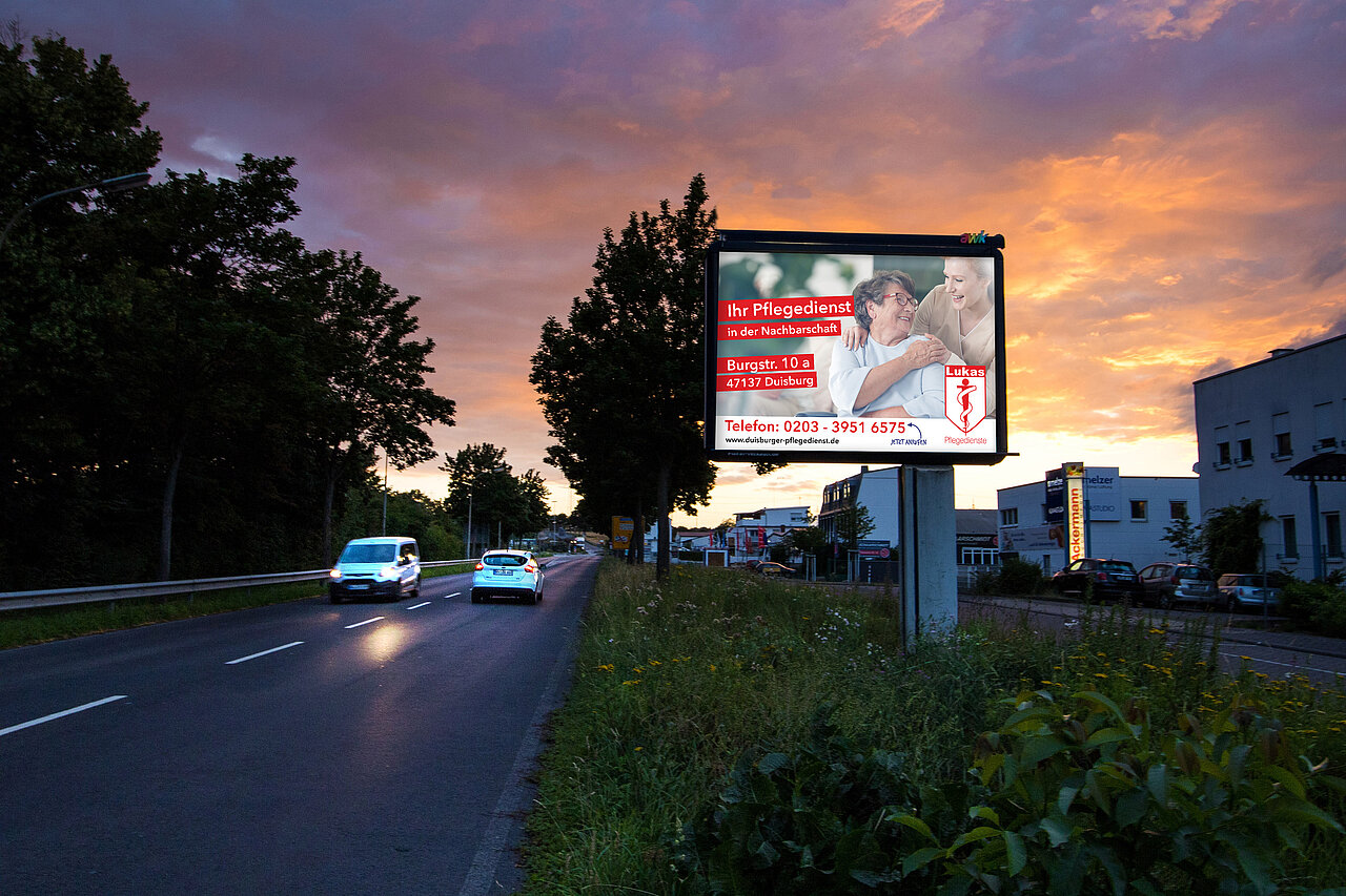 Großplakat mit 9 qm Werbefläche steht an befahrener Straße mit Pflegedienst-Motiv