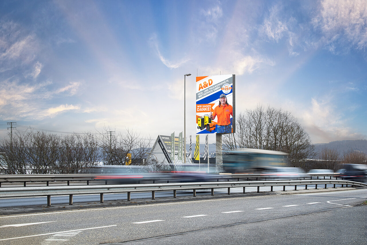 Digitaler Werbe-Tower am Straßenrand mit A&D-Werbemotiv, vorbeifahrenden Autos und offenem Himmel im Hintergrund