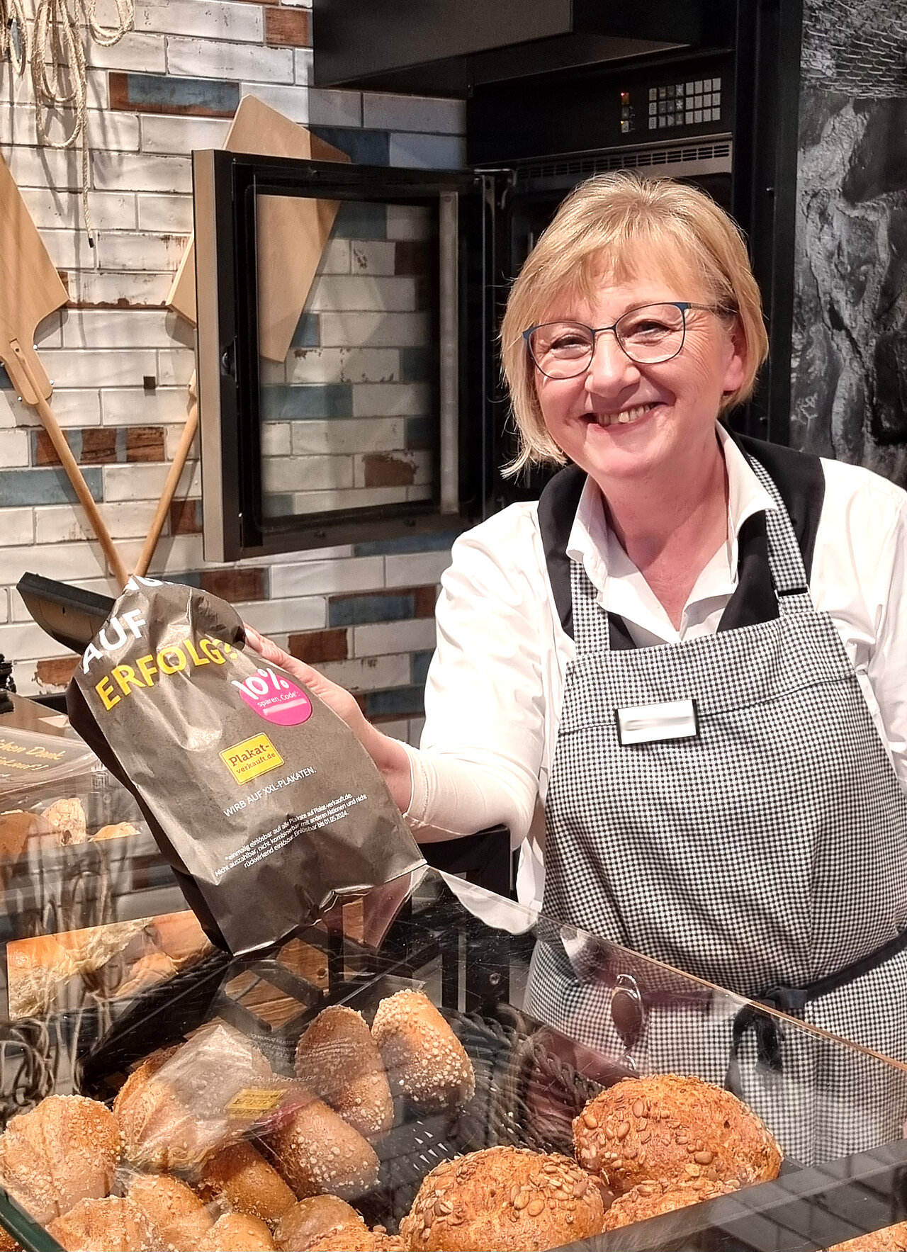 Bäckereimitarbeiterin reicht eine bedruckte Ambient Media Brötchentüte über die Verkaufstheke