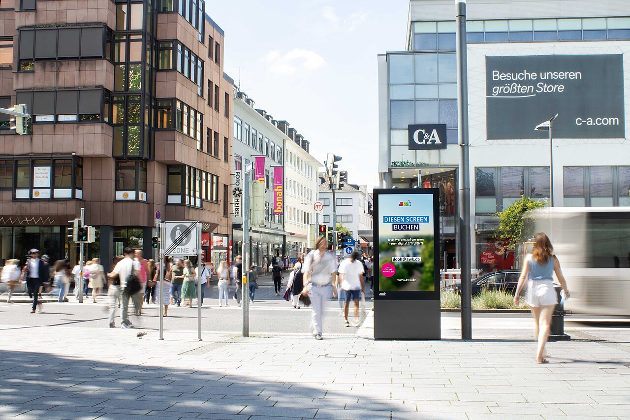 Digitales Citylight-Poster an einer belebten Einkaufsstraße mit vielen Passanten und Verkehr, die eine Werbung auf einem stehenden Screen im öffentlichen Raum zeigt.