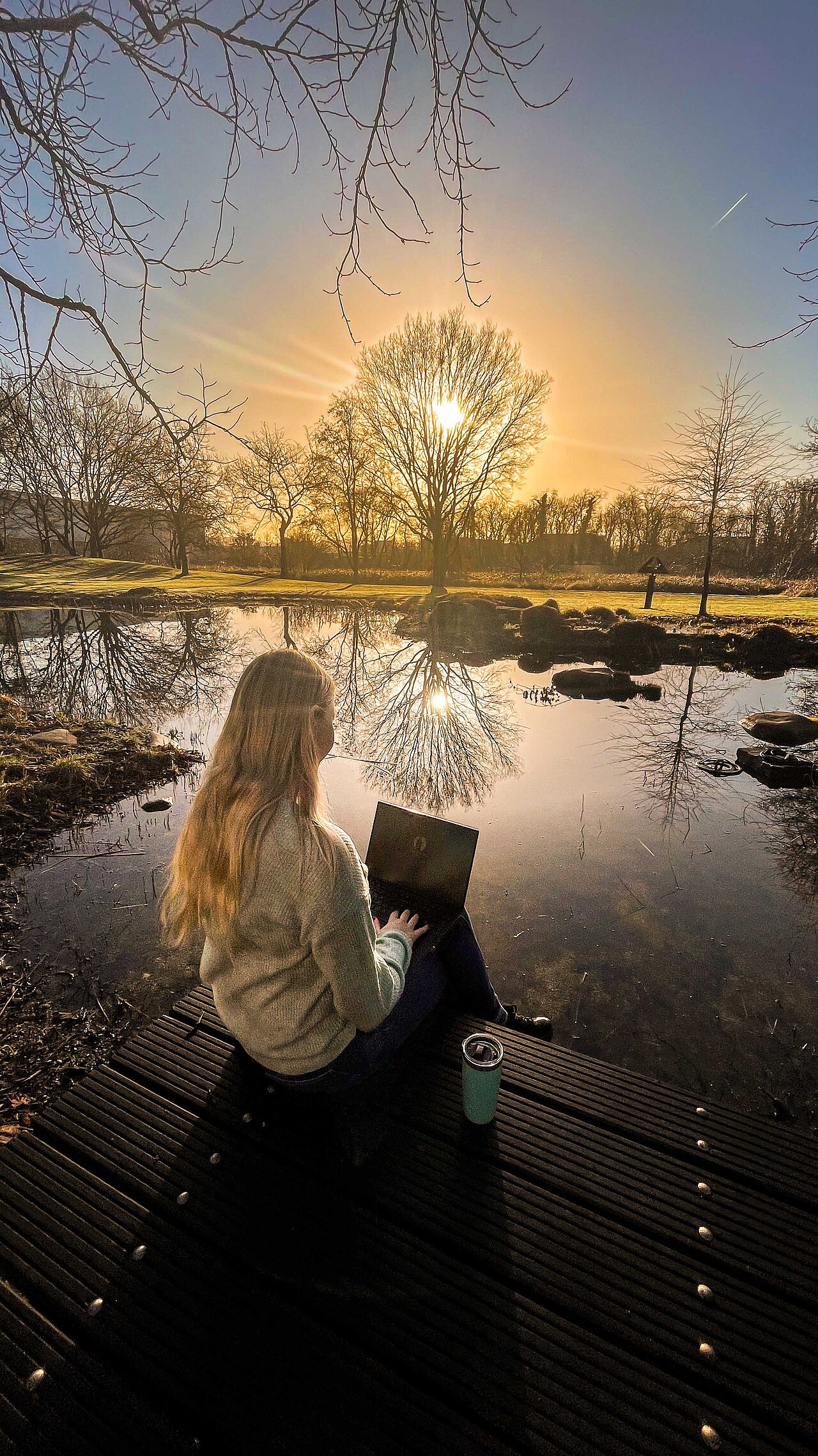 Mitarbeiterin sitzt mit Laptop am Teich auf dem Firmengelände von Plakat-verkauft.de