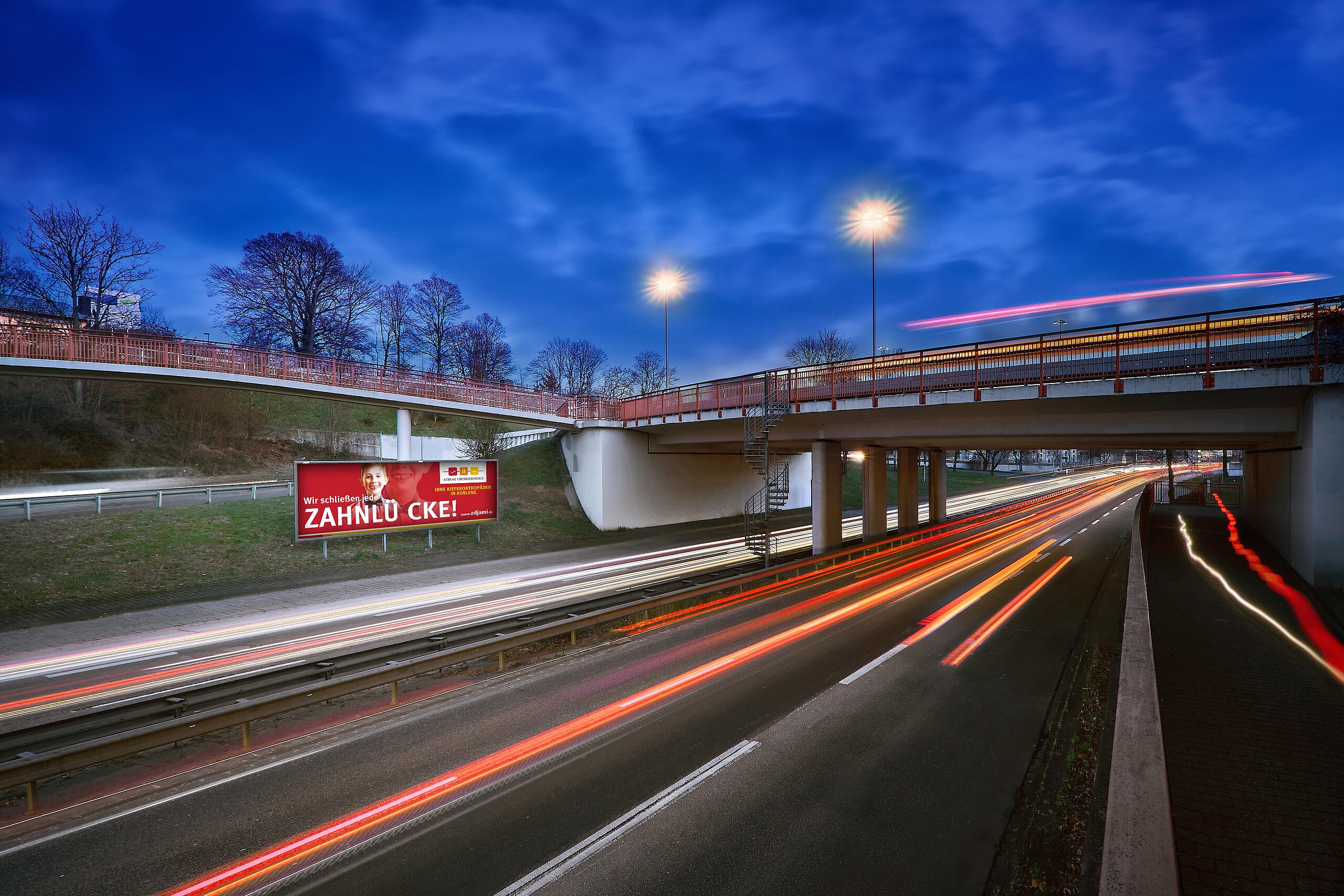 Großfläche mit Aufschrift „Wir schließen jede Zahnlücke“ an Schnellstraße bei Abenddämmerung