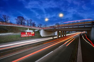 Großfläche mit Aufschrift „Wir schließen jede Zahnlücke“ an Schnellstraße bei Abenddämmerung