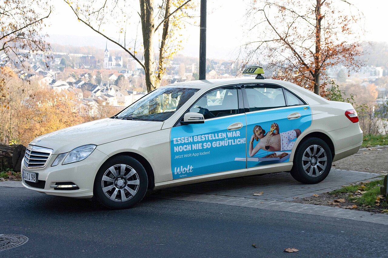 Wolt Taxiwerbung auf einem Mercedes-Benz in einer ruhigen Umgebung. Werbeaktion für bequeme Essensbestellung mit der Wolt App.