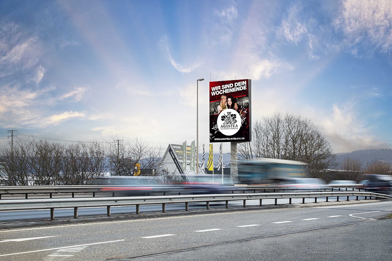 Digitaler Tower mit Werbung der Agostea-Eventlocation an einer viel befahrenen Straße, vorbeifahrende Autos und winterliche Umgebung im Hintergrund.