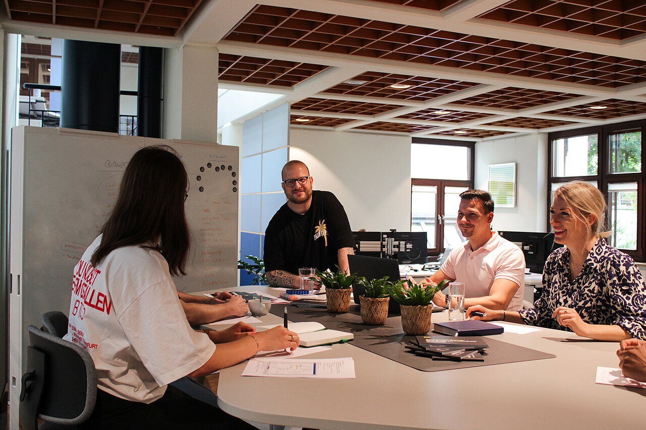 Team von Plakat-verkauft.de bei einem kreativen Meeting im Büro, lachend und im Austausch