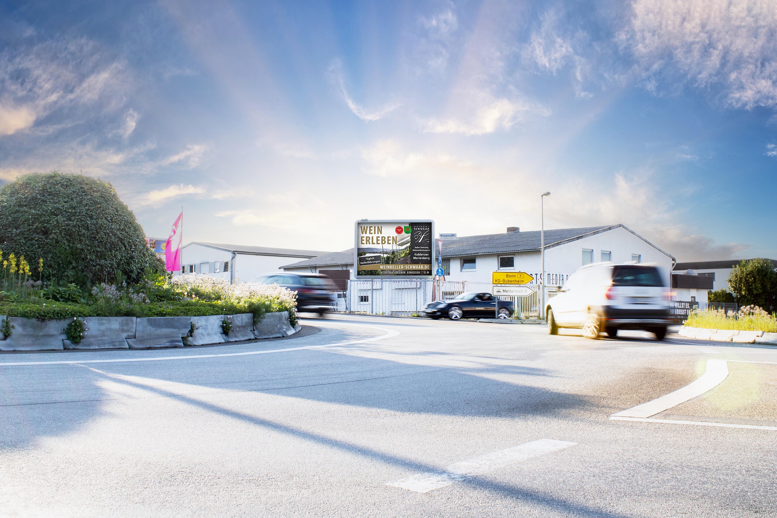 Plakat mit Aufschrift „Wein erleben“ an Kreisverkehr bei Sonnenschein