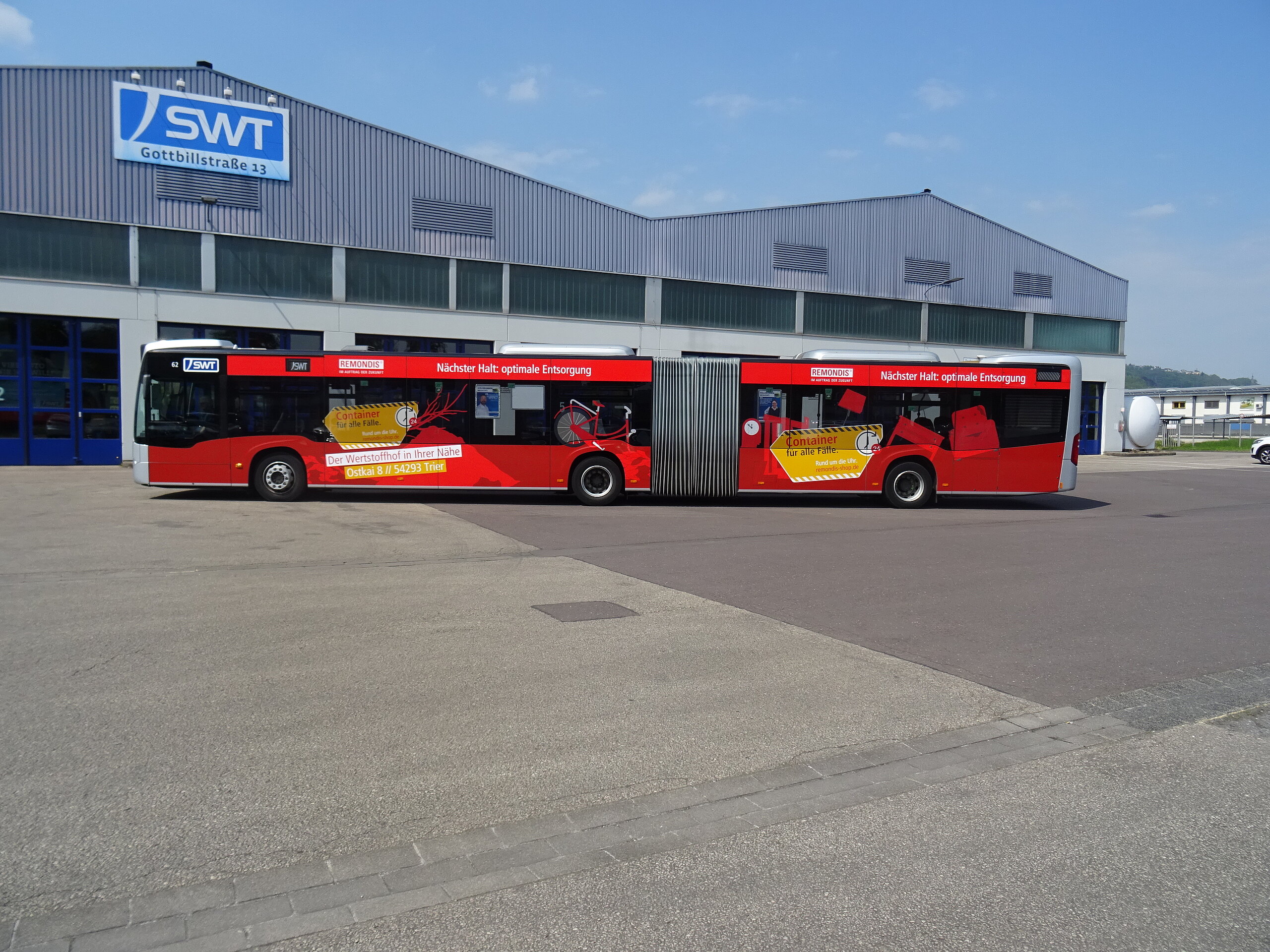 Ganzgestaltung auf einem Bus von 12 Monds, das für Containerlösungen wirbt, mit auffälliger roter Farbgestaltung und dem Slogan „Nächster Halt: optimale Entsorgung.“