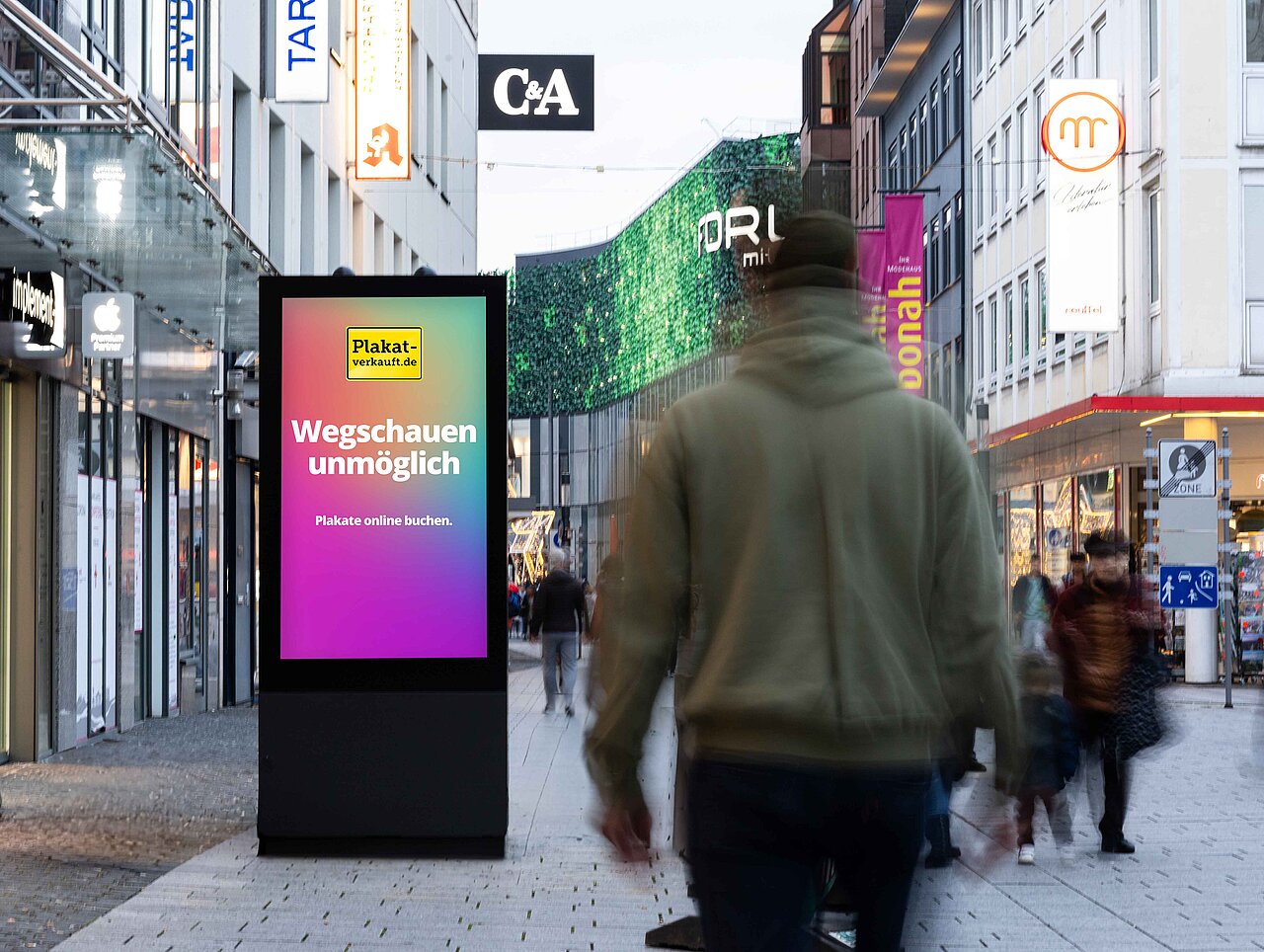 Digitale Werbevitrine in einer belebten Innenstadt, zeigt das farbige Motiv „Ignorieren unmöglich“, umgeben von Passanten und Verkehr an einer städtischen Kreuzung.
