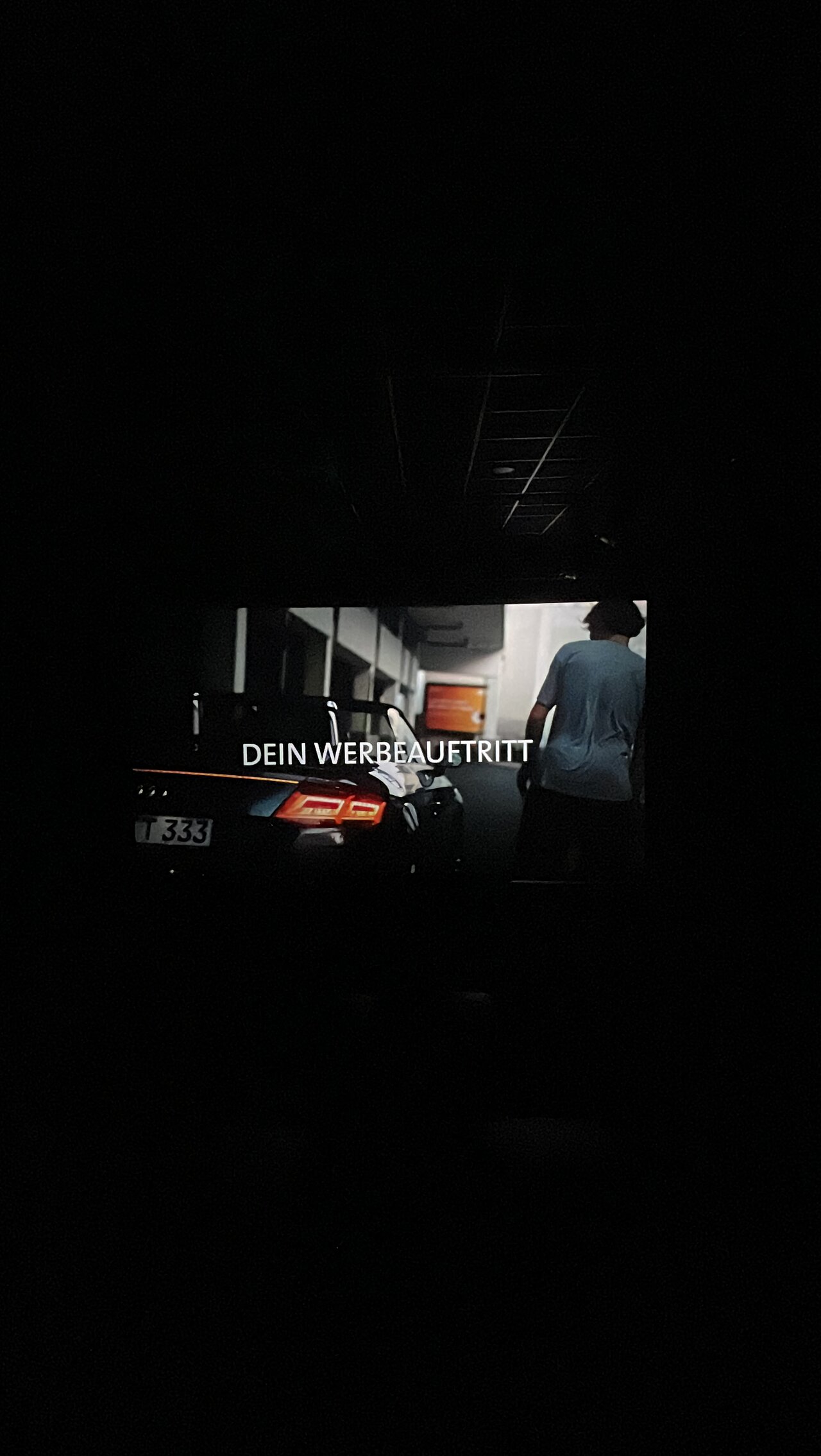 Kinospot im Kino mit dem Slogan 'DEIN WERBEAUFTRITT' auf der Leinwand. Eine Szene aus dem Film, die den Beginn eines Werbeauftritts zeigt.