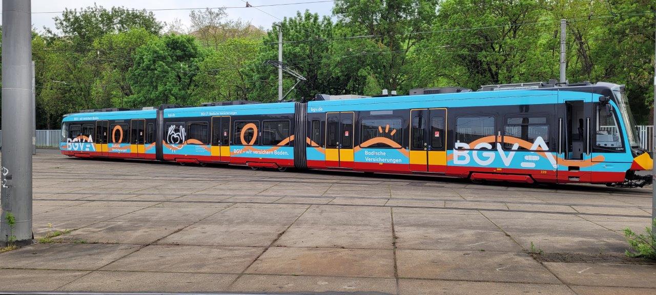 Straßenbahn mit farbenfroher Vollbeklebung des BGV im Depot, großflächige Bahnwerbung in Blau-Orange, die unterwegs hohe Aufmerksamkeit erzeugt.