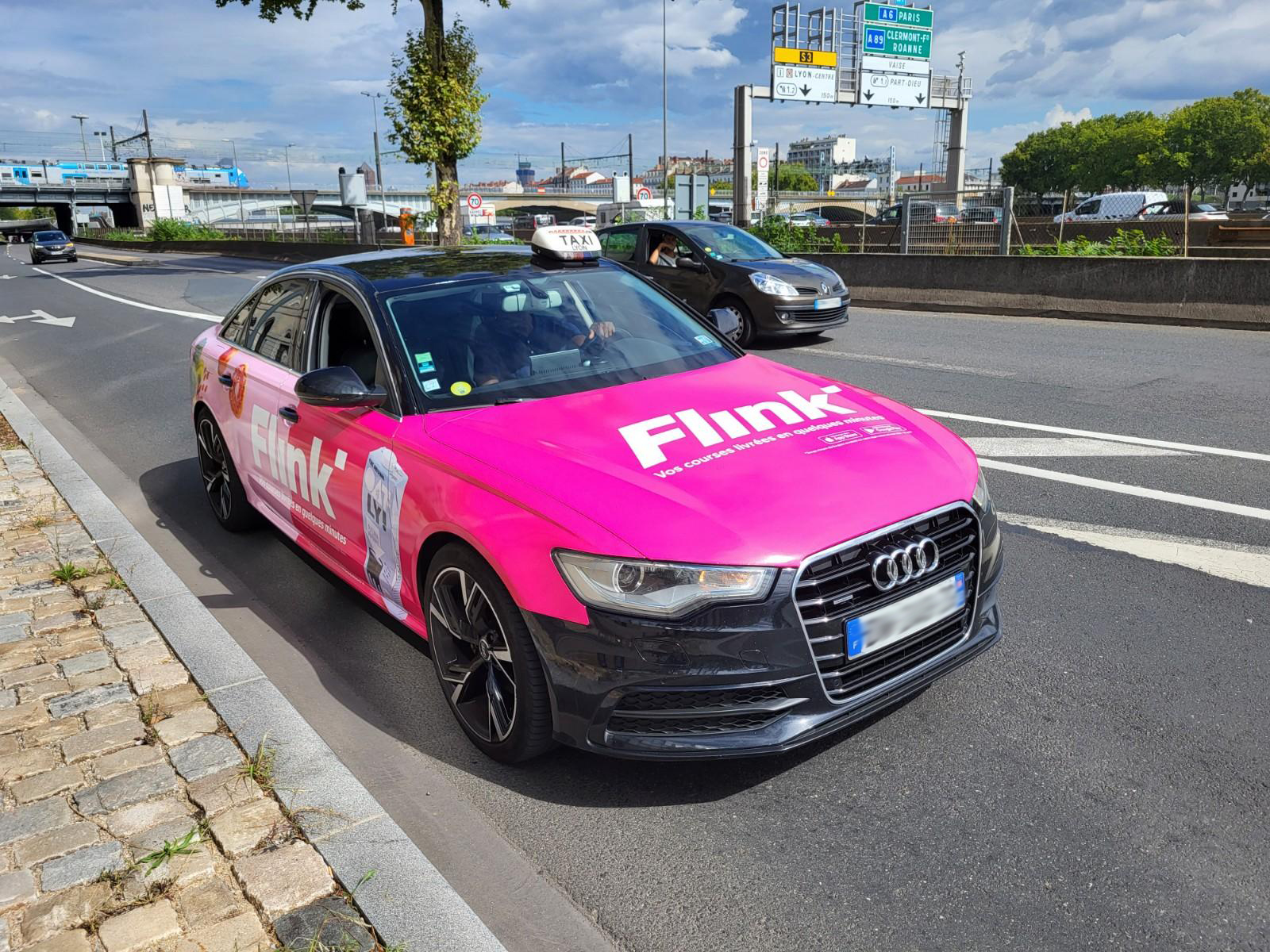 Flink Taxiwerbung auf einem Audi, der in der Stadt fährt. Auffällige pinke Werbung für schnelle Lebensmittel-Lieferung, die für maximale Sichtbarkeit sorgt.